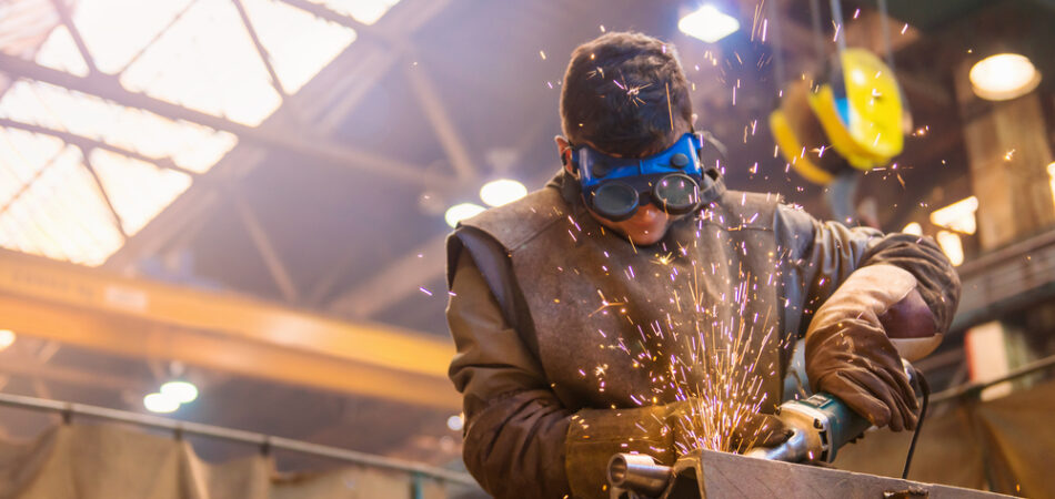 Young,man,with,protective,goggles,welding,in,a,factory